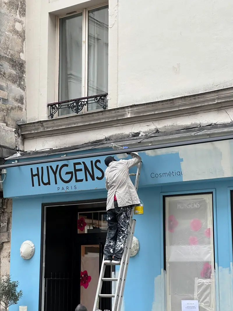 Peintre en bâtiment sur échelle réalisant la peinture d'une façade commerciale